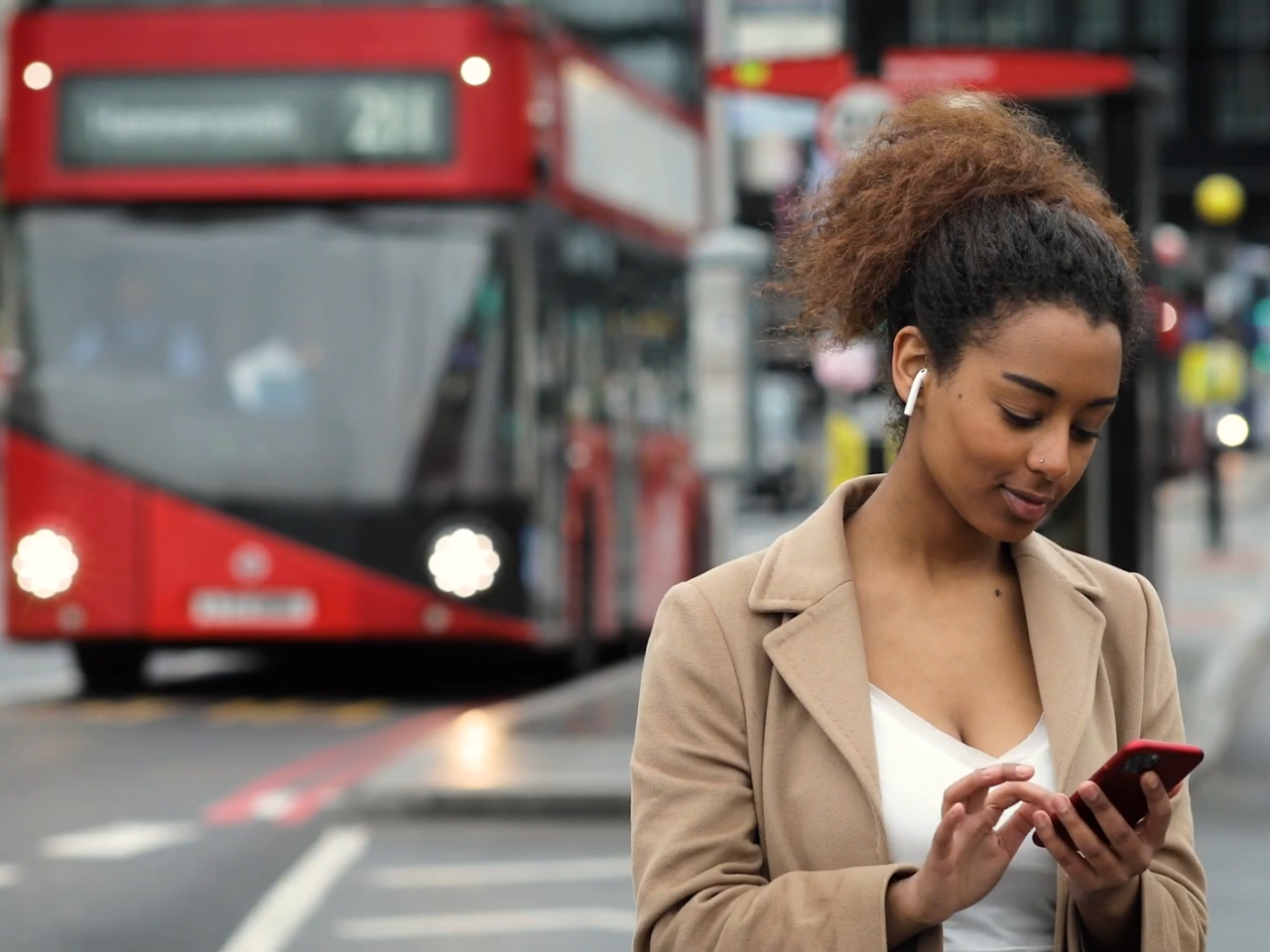 Person wearing wireless earbuds while using a phone with a red buss